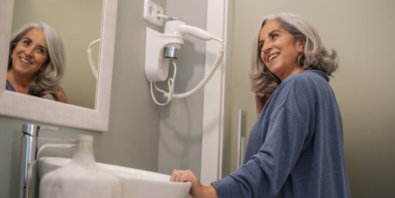 Senior Woman at Bathroom Sink Looking in Mirror at an Assisted Living Facility
