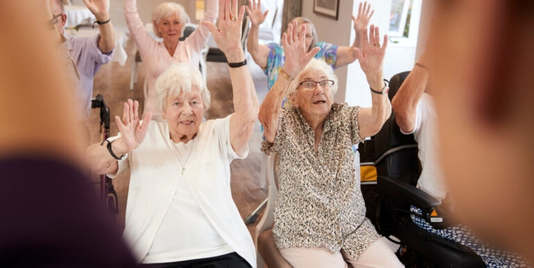 Elderly Women Raising Arms during a Seated Chair Yoga Class at Assisted Living Facility